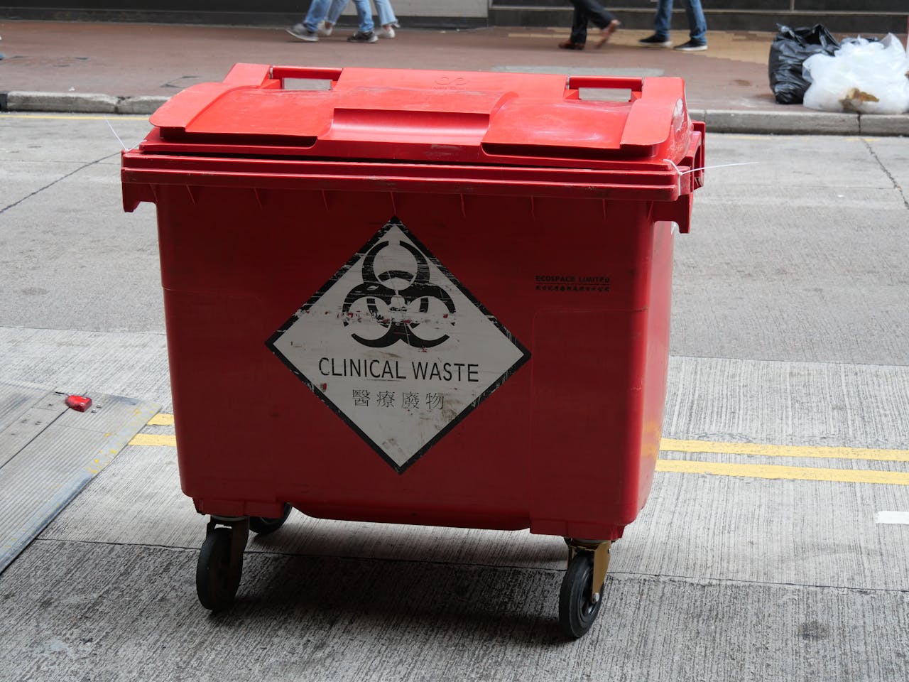 wheeled-trash-bin-on-the-street-10058479 A red wheeled bin labeled for clinical waste management on a city street.